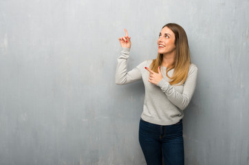 Young woman on textured wall pointing with the index finger and looking up