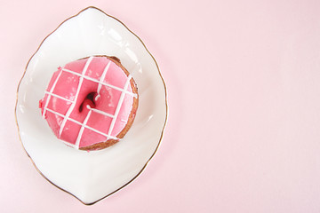 bright pink donut with white stripes on a white plate in the form of a leaf with a gold edging on a pink background. copy space..