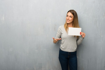 Young woman on textured wall holding an empty placard for insert a concept