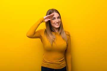 Young woman on yellow background saluting with hand
