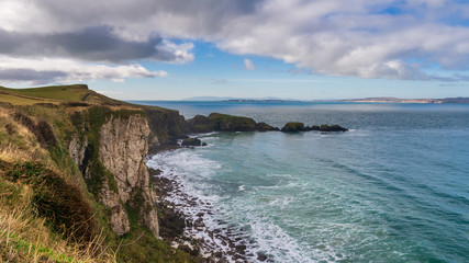 Fototapeta na wymiar Stunning rugged coastal landscape with sheer cliffs rising from the Atlantic Ocean waters under a dramatic winter day sky. County Antrim scenic coastline, Northern Ireland