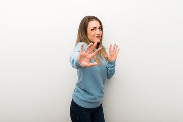 Blonde woman on isolated white background is a little bit nervous and scared stretching hands to the front