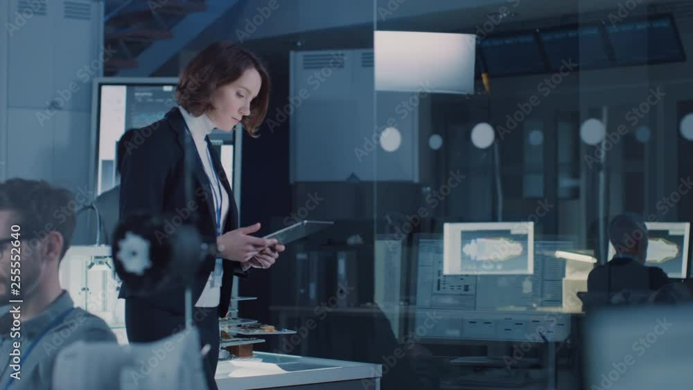 Poster In Technology Research Facility: Female Project Manager Walks Through the Lab Uses Tablet Computer. Team of Industrial Engineers, Developers Work on Engine Design Use Digital Whiteboard and Computers
