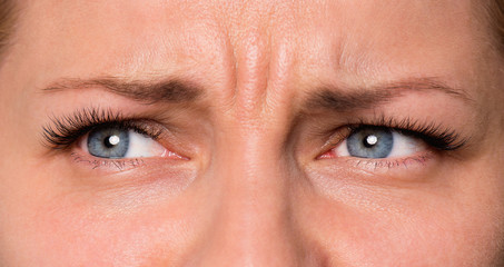 Close-up sad face of beautiful young woman with beautiful blue or gray eyes and big pretty eyelashes and eyebrows. Macro of human eyes - unhappy or scared, looking at camera.
