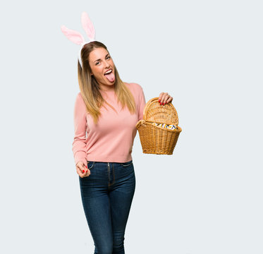 Young woman wearing bunny ears for Easter holidays showing tongue at the camera having funny look on isolated grey background
