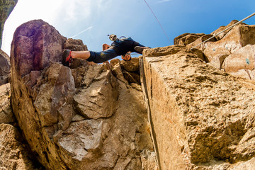 Climber Extreme climbs a rock on a rope with the top insurance, against the blue sky, bottom view