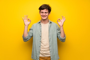 Teenager man over yellow wall in zen pose