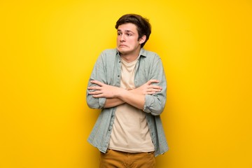 Teenager man over yellow wall making doubts gesture while lifting the shoulders