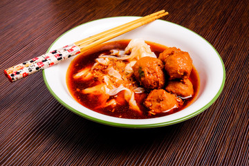 Indonesian famous foodstreet bakso / meatballs in a white bowl served with kuey teow on the table.