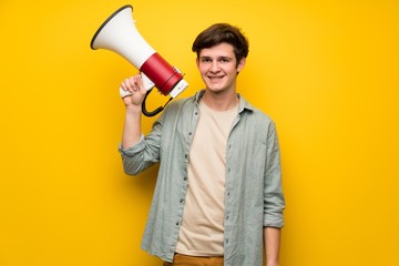 Teenager man over yellow wall holding a megaphone