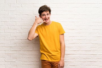 Teenager man over white brick wall making phone gesture. Call me back sign