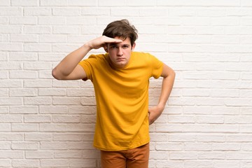Fototapeta premium Teenager man over white brick wall looking far away with hand to look something
