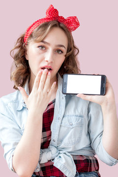 Beautiful young woman with pin-up make-up and hairstyle over pink background with mobile phone with copy space