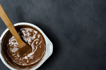Cake pan with chocolate batter and wooden spoon close up on dark stone background. - obrazy, fototapety, plakaty
