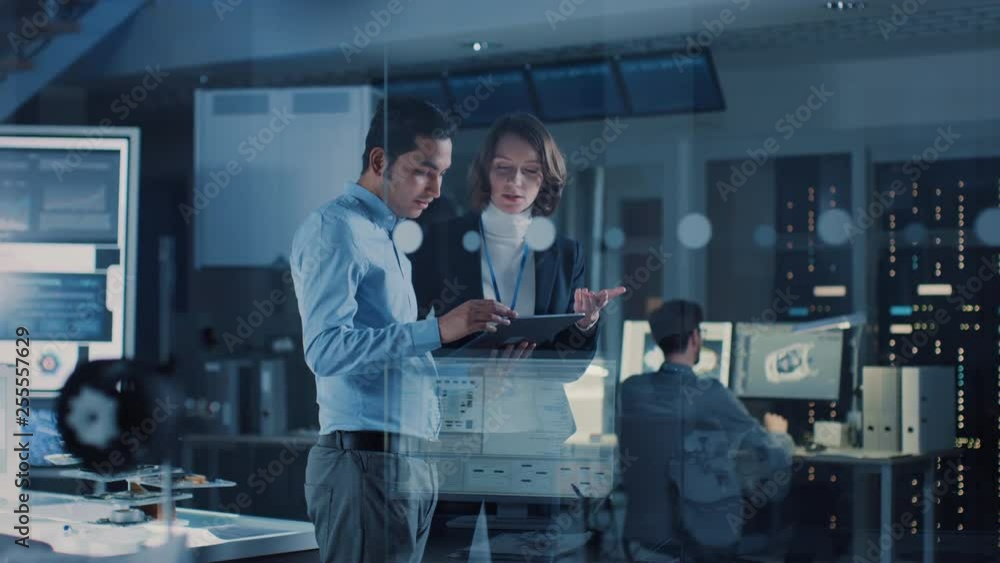 Aufkleber In Technology Research Facility: Female Project Manager Talks With Chief Engineer, they Consult Tablet Computer. Team of Industrial Engineers, Developers Work on Engine Design Using Computers