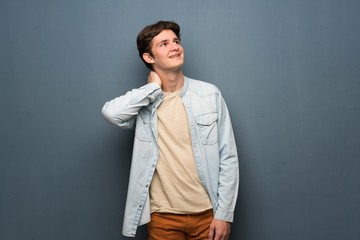 Teenager man with jean jacket over grey wall thinking an idea while scratching head