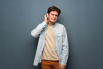 Teenager man with jean jacket over grey wall having doubts