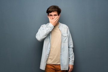Fototapeta premium Teenager man with jean jacket over grey wall covering mouth with hands for saying something inappropriate