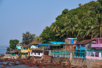 Sunny landscape of the coastal line on the background of palm trees and jungle with a steep slope. Beautiful  horizontal photo taken around the sea, houses, palm trees, stones, and blue sky