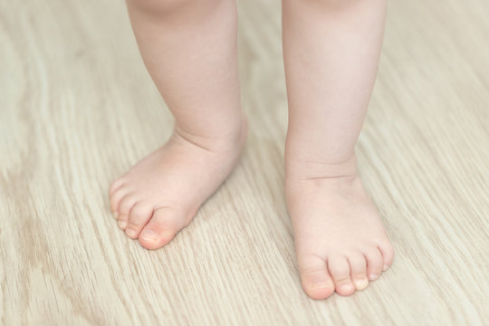 Baby's Feet, First Step, Close Up.Healthy Foot Baby. Feet Of Baby's Naked Against The Background Of The Wooden Floor