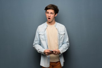 Obraz premium Teenager man with jean jacket over grey wall surprised and sending a message