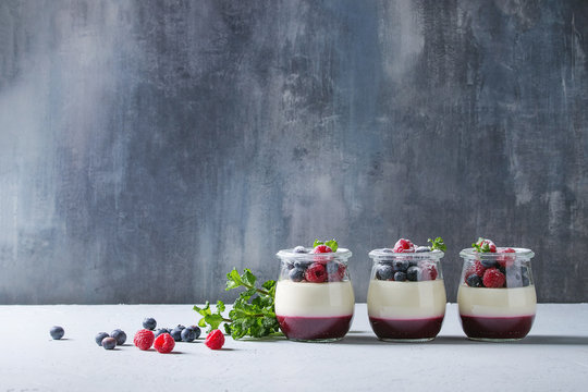 Homemade classic dessert Panna cotta with raspberry and blueberry berries and jelly in jars, decorated by mint and sugar powder over white blue table