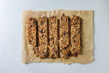 Cutting homemade energy oats granola bars with dried fruits and nuts on baking paper over white texture background. Healthy snack. Flat lay, space