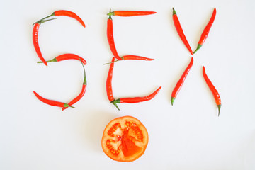 Red hot chili peppers and half a tomato on a white surface laid out the word Sex. Seasoning and health
