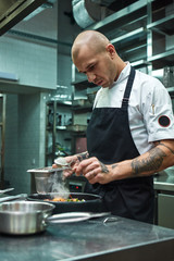 Need more spices. Vertical photo of restaurant chef with several tattoos adding a special spice to fresh cooked pasta Carbonara.