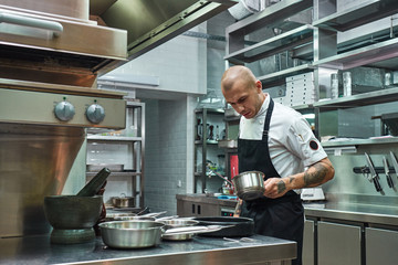 Sauce is ready. Handsome and confident chef in apron, with several tattoos on his arms holding a bowl with his famous sauce