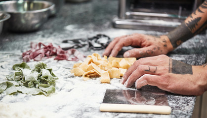 Family recipe. Close-up photo of male chef's hands with tattoos finishing making italian pasta on the kitchen table with flour