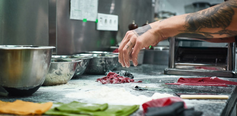 Cooking moments. Cropped image of chef's hands with beautiful tattoos making traditional italian pasta in restaurant kitchen