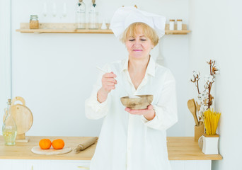 Beautiful senior woman in cook cap with a wooden pot at home in the kitchen