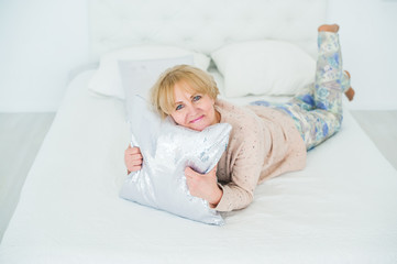 Smiling older woman resting in the bedroom, embracing pillow