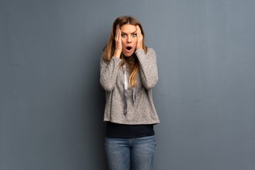 Blonde woman over grey background surprised and shocked while looking right