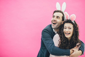 Young happy couple standing on pink background. With a hook on the head. Hugging his wife, the man...