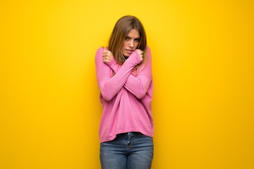 Woman with pink sweater over yellow wall freezing