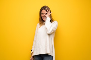 Blonde woman over yellow wall makes funny and crazy face emotion