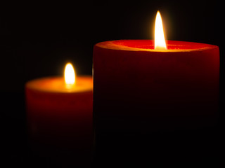 Two red candles in the dark. Flame is a beautiful yellow. Candles illuminate each other in the dark.