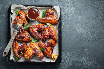 Roasted chicken wings in barbecue sauce with sesame seeds and parsley in a baking tray on a dark table. Top view with copy space. Tasty snack for beer on a dark background. Flat lay