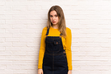 Teenager girl over white brick wall with sad and depressed expression