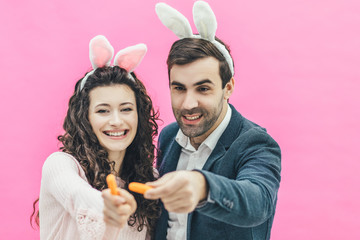 Young beautiful couple standing on a pink background. During this man and his wife hold small...