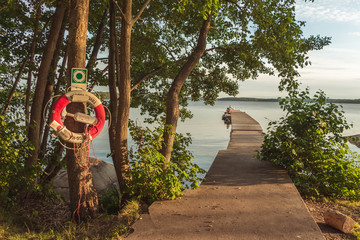 A young girl and a fisherman boy on the pier on sunset. Natural silence and idyll in the city. Symbol of salvation, protection and security. Calm landscape. Lifebuoy hanging on trunk of the tre