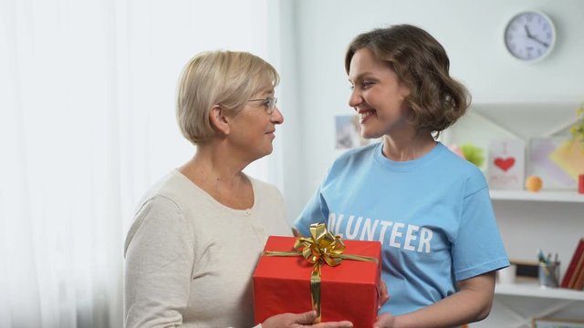Happy woman in volunteer t-shirt giving gift box to aged lady, holiday charity