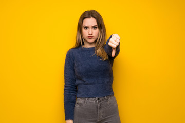 Teenager girl over yellow wall showing thumb dowg with negative expression
