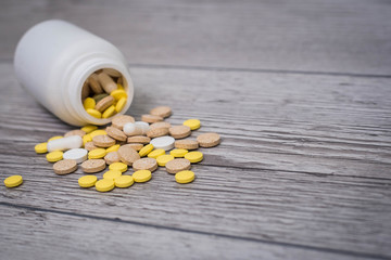 White, yellow and pink pills spilling out of a toppled bright white pill bottle. Medical colorful pills, capsules or supplements for the treatment and health care on wooden background.