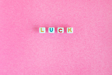 Word "Luck" made out of beads on pink background