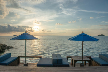 Fototapeta premium Rest on the tropical coast. Umbrellas and two empty lounge chairs stand on a wooden deck near the sea