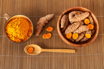 Turmeric roots and powder in bowls on bamboo background. Top view