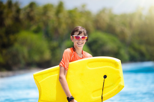 Child surfing on tropical beach. Surfer in ocean. - Powered by Adobe